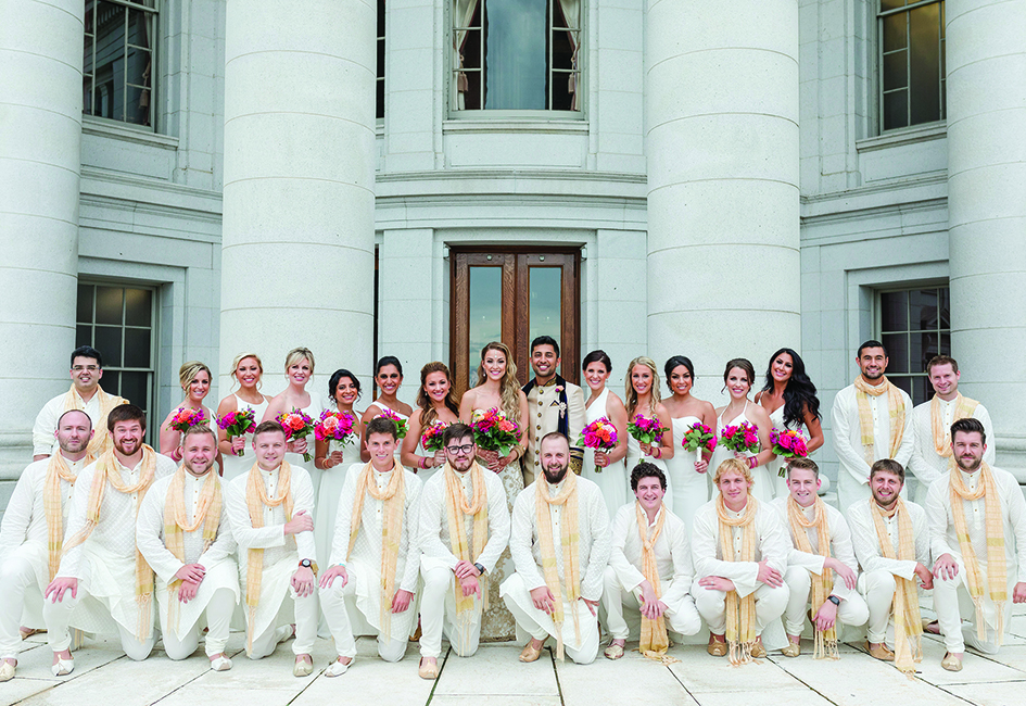 Molly Stiffler and Bobby Syal pose with their wedding parties. The groom and groomsmen wear traditional Indian dress.