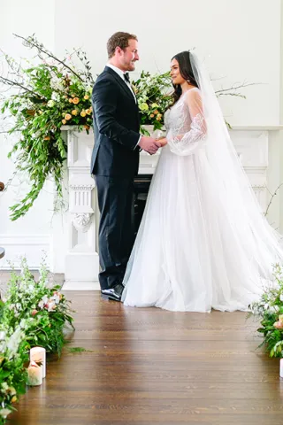 A bride and groom stand in the aisle at the Covenant at Murray Mansion amid their orange, gold and peach wedding flowers