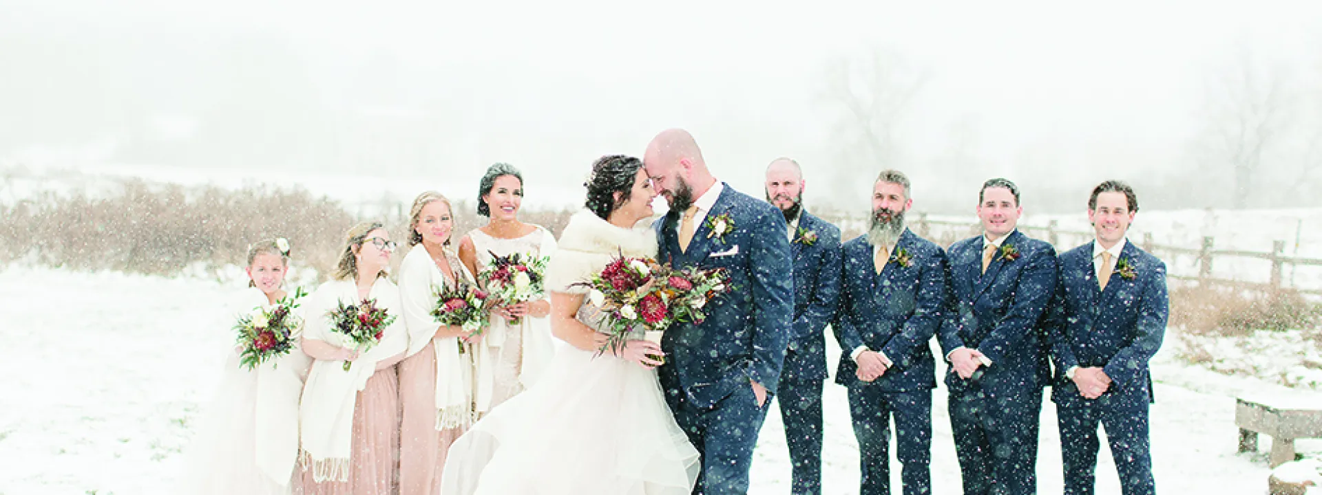 Maggie Christie and Jeremy Kocher kiss in front of their wedding party at The Enchanted Barn.